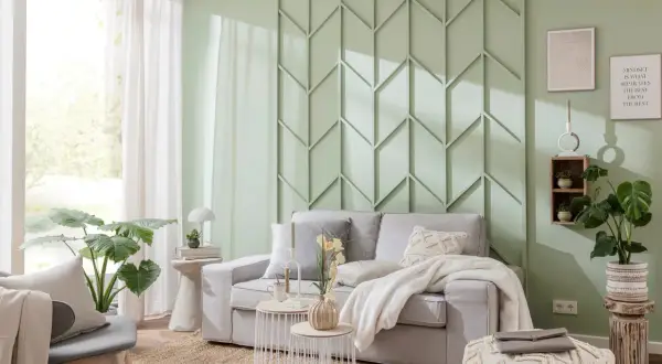 Eine stilvolle Wand hinter der Couch gestalten mit einem geometrischen Paneel in Mintgrün. Gemütliche Atmosphäre mit hellgrauem Sofa, Kissen und Decke.