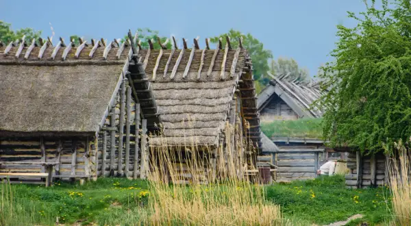 Drewniane chaty kryte strzechą, jak w skansenach w Polsce, stoją nad wodą.