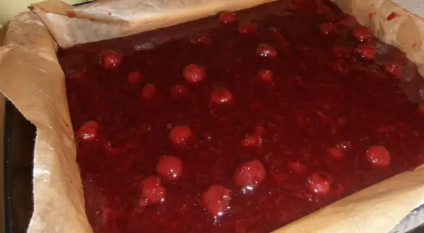 Gotowe do pieczenia ciasto bajka z wiśniami w blaszce wyłożonej papierem. Słodka, czerwona masa z całymi owocami.