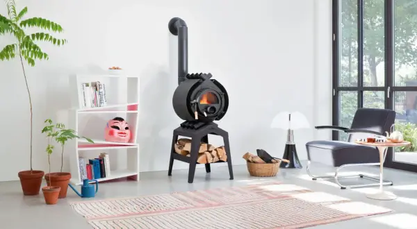 Ein gemütliches Wohnzimmer mit einem Bullerjan B3 Keramik Ofen, der Holzscheite wärmt. Daneben ein Bücherregal mit einer bunten Maske.