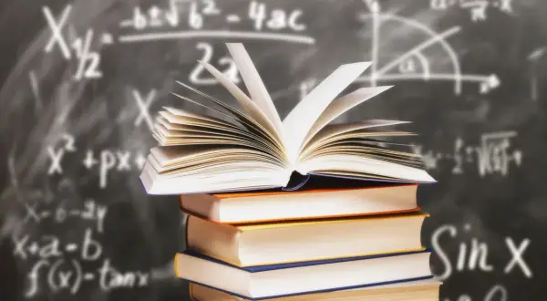Stos książek z otwartą księgą na wierzchu na tle tablicy z równaniami matematycznymi.