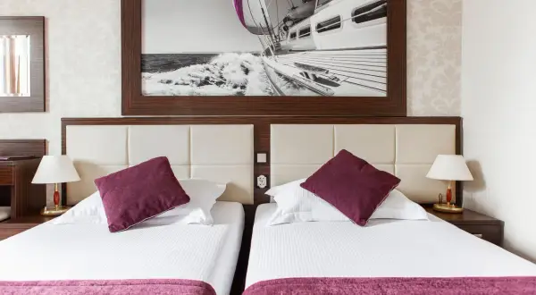 Dwie wygodne łóżka w pokoju hotelowym, nad nimi obraz z żaglówką. Idealne miejsce na wypoczynek, jak sugerują primavera jastrzębia góra opinie.