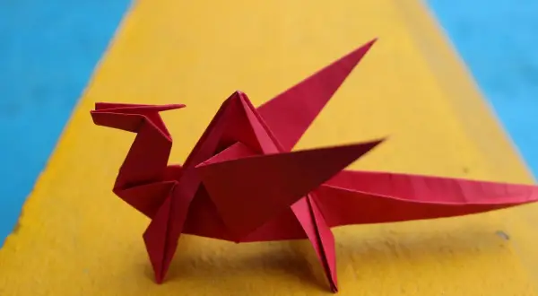 Un dragón rojo de papiroflexia fácil descansa sobre una superficie amarilla y azul.