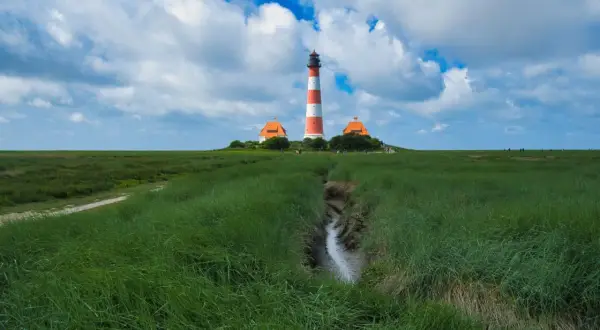 Leuchtturm Westerheversand, ein ikonischer fotospot in Schleswig-Holstein, ragt über grünes Marschland unter dramatischem Himmel.