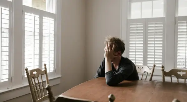 Uomo seduto a un tavolo, con la mano sul viso, immerso in pensieri profondi. Un momento di introspezione, dove mettersi in discussione è parte del percorso psicologico.