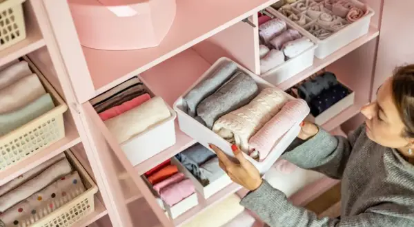 Una mujer organiza su armario, doblando ropa en contenedores. Aprende como ordenar un armario para tener todo a la vista y ordenado.
