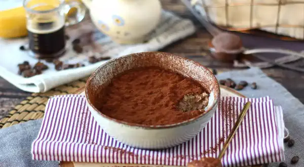 Schüssel mit Tiramisu Overnight Oats, bestäubt mit Kakao. Ein Löffel mit dem Dessert liegt daneben.
