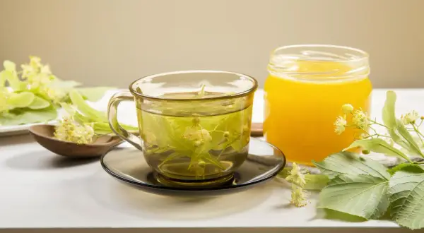 Aromatyczna herbata z lipy w szklance, obok słoik miodu i świeże kwiaty lipy.