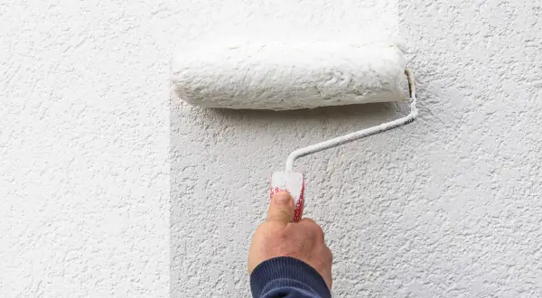 Hand rollt weiße Farbe auf eine strukturierte Wand. Die Frage, welche Wandfarbe deckt am besten, wird hier visuell beantwortet.