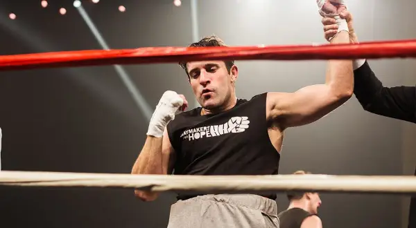 A boxer's arm is raised in victory, a moment of triumph in amateur vs professional boxing. The crowd roars as the referee declares the winner.