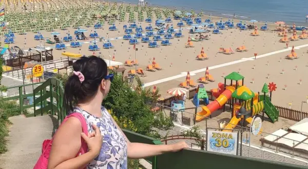 Donna con borsa rosa ammira la spiaggia di Gabicce Mare centro, con ombrelloni, lettini e un parco giochi colorato.
