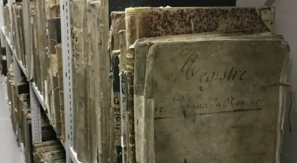 Des registres anciens, certains marqués "archive 07", s'alignent sur des étagères métalliques, témoins silencieux du temps.