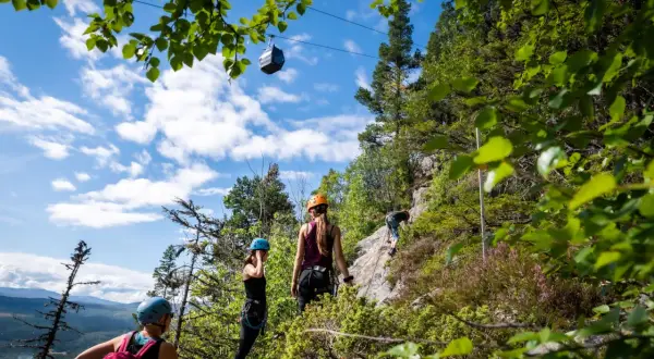 Äventyr vid Ramundberget: klättrare på klippvägg, linbana i skyn, vacker utsikt.