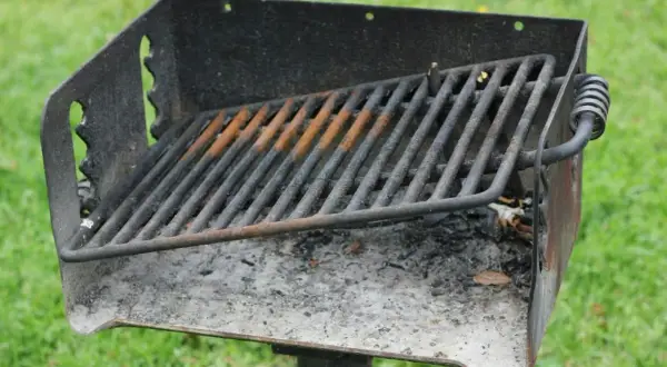Ett rostigt grillgaller med aska under, redo för nästa grillkväll i parken.