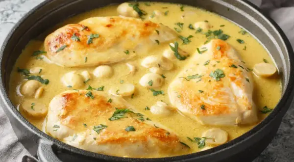 Aromatyczna potrawka z kurczaka w kremowym sosie z pieczarkami, posypana świeżą natką pietruszki, podana w czarnym naczyniu.