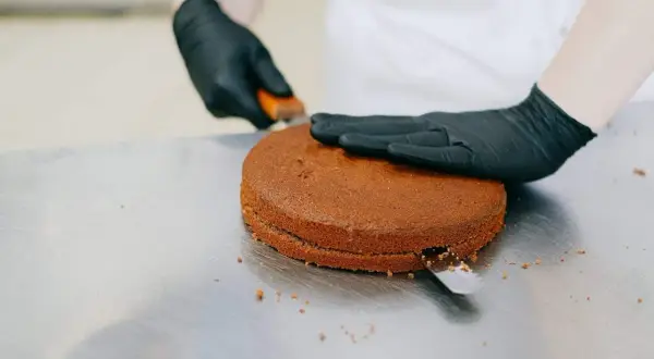 Manos enguantadas cortan un bizcocho redondo, preparándolo para ser la base de una deliciosa masa de tarta.