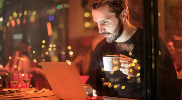 Mężczyzna z kubkiem kawy pracuje na laptopie, szukając informacji o tym, jaki internet do domu bez światłowodu będzie najlepszy.