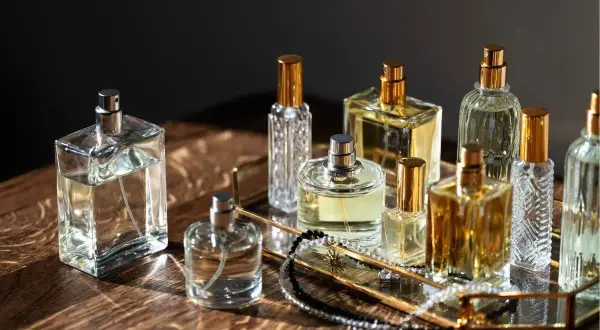 Kolekcja flakonów perfum, w tym Estee Lauder Modern Muse, na złotej tacy z biżuterią.
