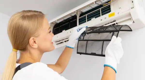 Kobieta w białych rękawiczkach wyjmuje filtr z klimatyzacji domowej. Dba o czyste powietrze.