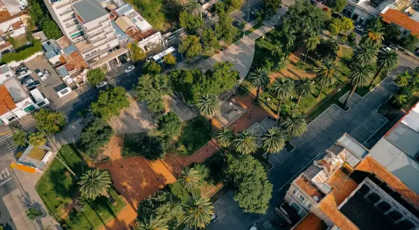 Un parco urbano rigenerato, con palme e alberi, circondato da edifici residenziali e commerciali.