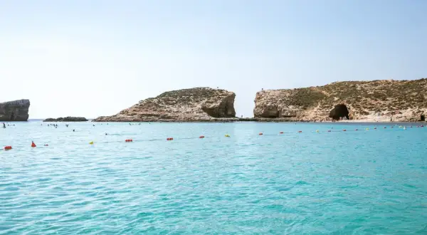 Turkusowa woda, skaliste klify i plaża z ludźmi. Idealne miejsce na wakacje, zastanawiasz się, ile leci się na Maltę?