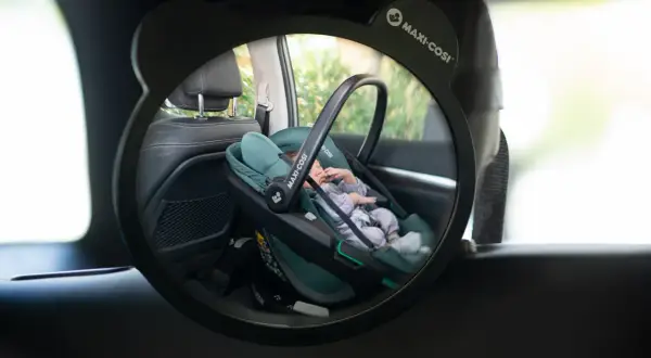 Ein Baby schläft friedlich in einer grünen Maxi-Cosi Babyschale im Rückspiegel eines Taxis.