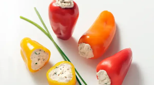 Des mini poivrons farcis colorés, garniture crémeuse et herbes fraîches, prêts à être dégustés.