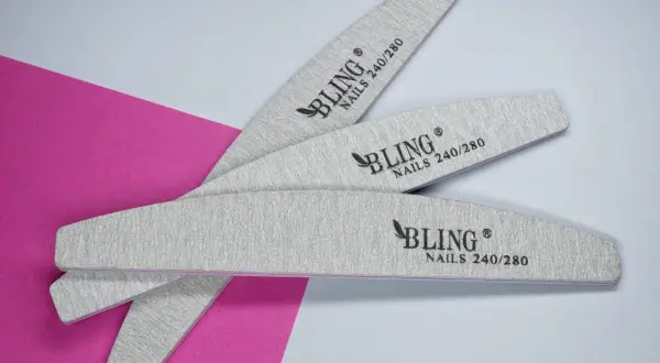 Trzy pilniki do paznokci naturalnych marki BLING o gradacji 240/280, ułożone na tle w kolorze różowym i białym.