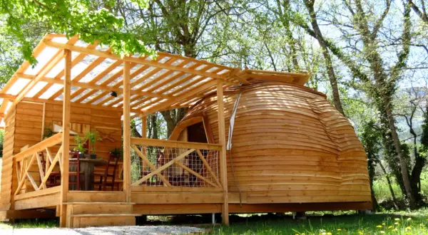 Cabane en bois et dôme de glamping Paca, avec terrasse et table extérieure, dans un cadre verdoyant.