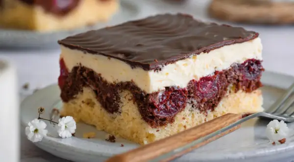 Ein Stück Donauwelle-Kuchen mit Schokoladenglasur, Sahne und Kirschen. Ein köstliches Rezept für den perfekten Genuss.