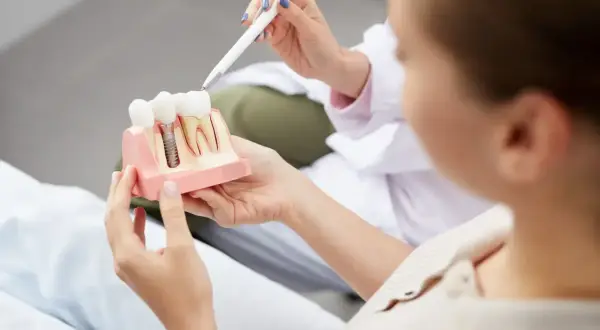 Dentysta wyjaśnia pacjentce budowę implantu zębowego, odpowiadając na pytanie: czy implanty są bezpieczne.