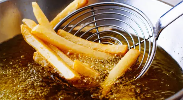 Patatine fritte dorate che sfrigolano nell'olio di oliva, pronte per essere gustate.