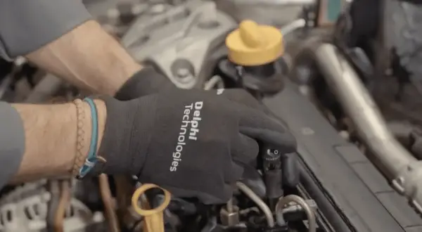 Manos con guantes negros trabajando en un motor diésel, manipulando un inyector.