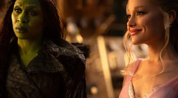 Ariana Grande in einem rosa Kleid und eine grün geschminkte Frau mit dunklen Zöpfen in einem dunklen Outfit. Szenen aus Filmen von Ariana Grande.