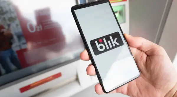 Dłoń trzyma smartfon z logo Blik. Kto wymyślił Blik? To polski system płatności mobilnych, który zrewolucjonizował transakcje.