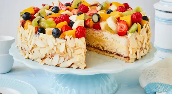 Eine einfache Torte, verziert mit frischen Früchten wie Erdbeeren, Kiwi und Blaubeeren, umgeben von Mandelblättchen.