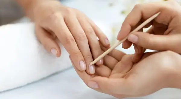 Delikatne dłonie poddawane zabiegowi manicure biologicznego. Skórki są starannie odsuwane patyczkiem, przygotowując paznokcie do dalszej pielęgnacji.