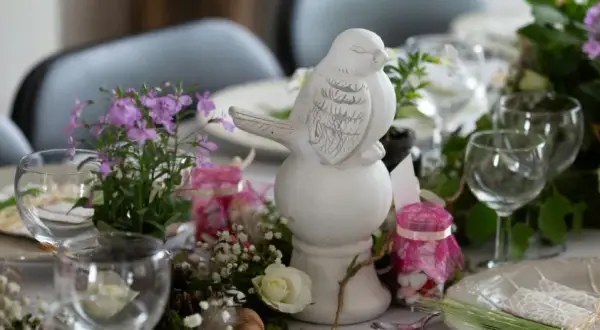 Décoration de table printanière avec un oiseau en céramique, fleurs et bougies roses. Idéal pour une célébration comme un baptême civil, une démarche simple et élégante.