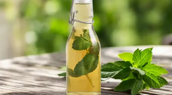 Bouteille de sirop de menthe maison avec des feuilles de menthe fraîche sur une table en bois.