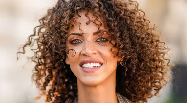 Mujer con rizos voluminosos y un estilo que evoca los peinados años 20. Su pelo rizado luce natural y lleno de vida.