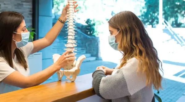 Fizjoterapeuta pokazuje pacjentce model kręgosłupa, wyjaśniając, jak wygląda dyskopatia lędźwiowa i przepuklina kręgosłupa.