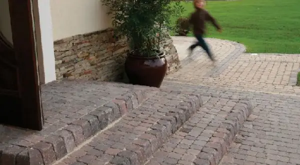 Schody z polbruku prowadzą do drzwi. W tle dziecko biegnie po trawniku.