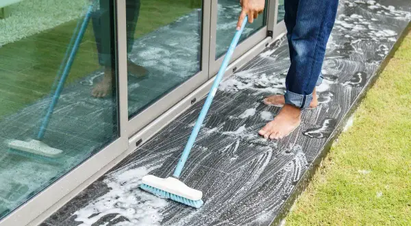 Persona a piedi nudi lava il marmo esterno annerito con una scopa e schiuma.