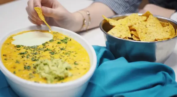 Salsa de queso cremosa con guacamole y nachos, una persona moja un totopo.