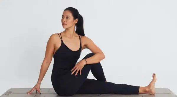 Mujer en postura de ardha matsyendrasana, girando el torso hacia la derecha, con la pierna izquierda flexionada y el pie derecho extendido.