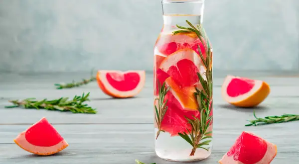 Erfrischendes Detox Wasser mit Grapefruit und Rosmarin in einer Glasflasche, umgeben von frischen Fruchtscheiben und Kräuterzweigen.