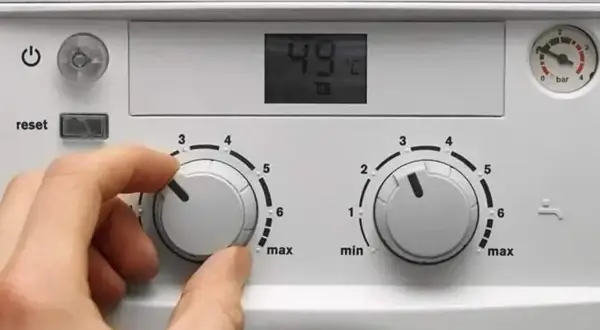 Dłoń kręci pokrętłem, ustawiając temperaturę pieca gazowego dwufunkcyjnego. Na wyświetlaczu 49°C.