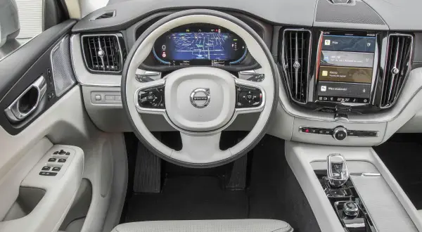 Wnętrze Volvo XC60 T6 z ekranem nawigacji i multimediów. Jasna tapicerka, biała kierownica z logo Volvo.