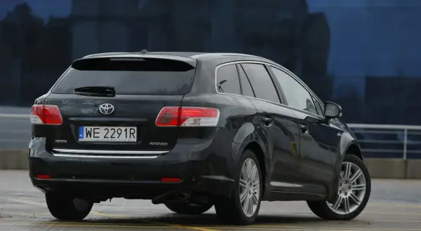 Czarna Toyota Avensis T27, kombi, z widocznym tyłem i tablicą rejestracyjną. Może być pomocna przy wymianie żarówki.