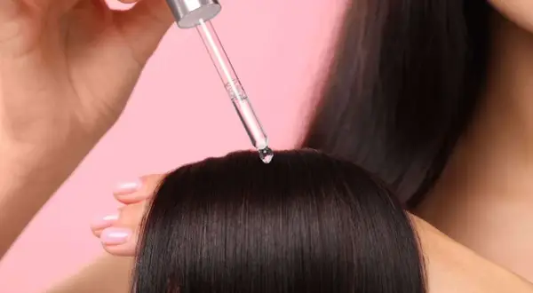 Une goutte de sérum tombe sur des cheveux bruns. Aide à choisir quel sérum choisir pour des cheveux brillants.
